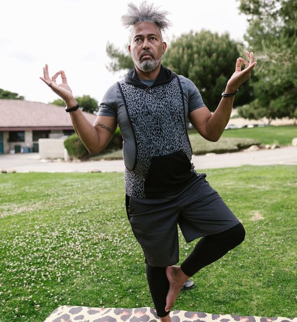 Smiling senior man standing in a simple yoga balance pose in a park.